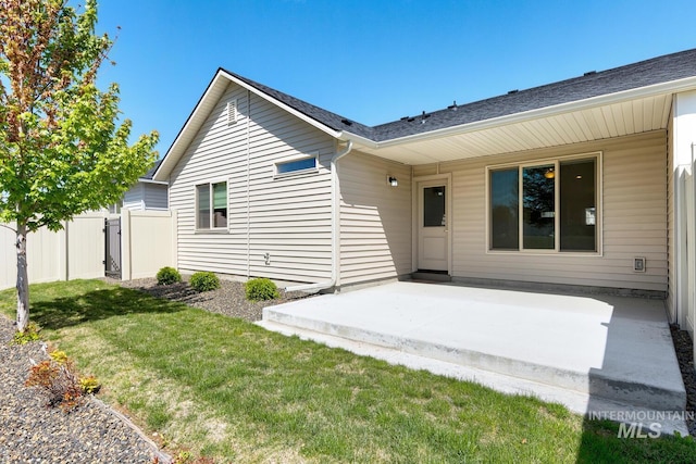 rear view of property featuring a patio, a lawn, fence, and roof with shingles
