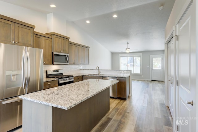 kitchen featuring a sink, stainless steel appliances, a peninsula, lofted ceiling, and tasteful backsplash