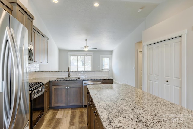 kitchen featuring a peninsula, tasteful backsplash, a sink, light wood finished floors, and appliances with stainless steel finishes