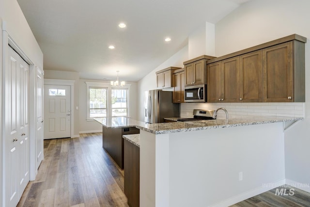 kitchen with tasteful backsplash, vaulted ceiling, a chandelier, light wood-style floors, and stainless steel appliances