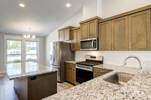 kitchen featuring vaulted ceiling, a sink, a chandelier, stainless steel appliances, and light wood-style flooring