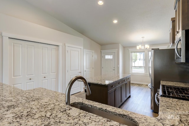 kitchen featuring wood finished floors, a sink, light stone counters, stainless steel microwave, and an inviting chandelier