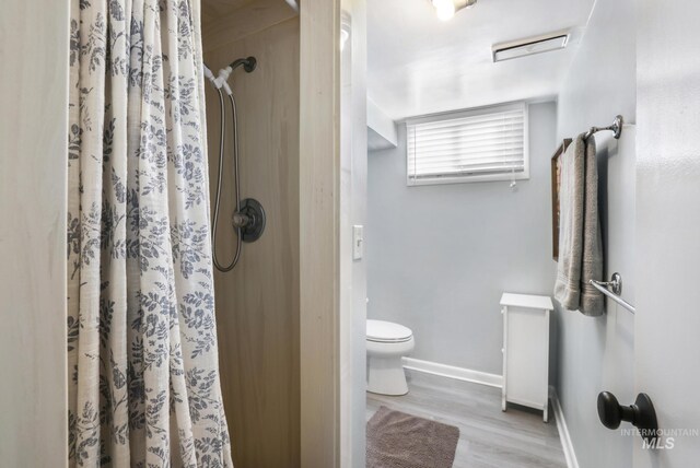 bathroom with toilet, a shower with shower curtain, baseboards, and wood finished floors