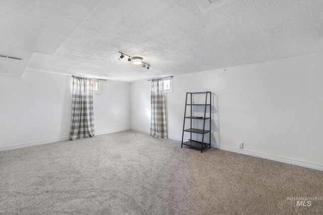 carpeted spare room featuring visible vents, a textured ceiling, and baseboards