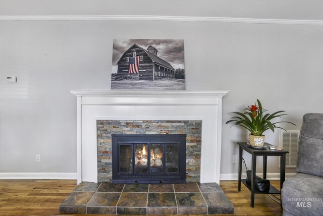 interior details with a glass covered fireplace, wood finished floors, baseboards, and ornamental molding