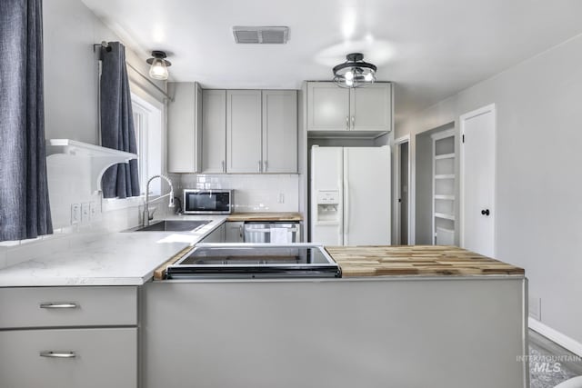 kitchen with stainless steel microwave, visible vents, gray cabinetry, decorative backsplash, and white fridge with ice dispenser