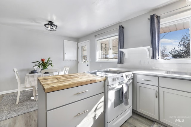 kitchen with butcher block countertops, tasteful backsplash, light wood finished floors, and white range with electric cooktop