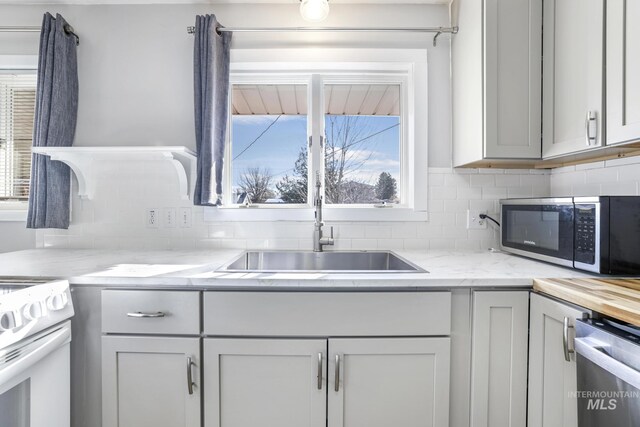 kitchen with a wealth of natural light, decorative backsplash, appliances with stainless steel finishes, and a sink