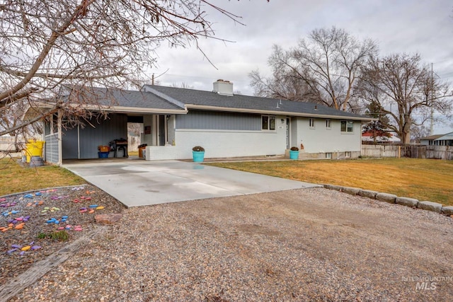 back of house featuring driveway, fence, a yard, brick siding, and a chimney