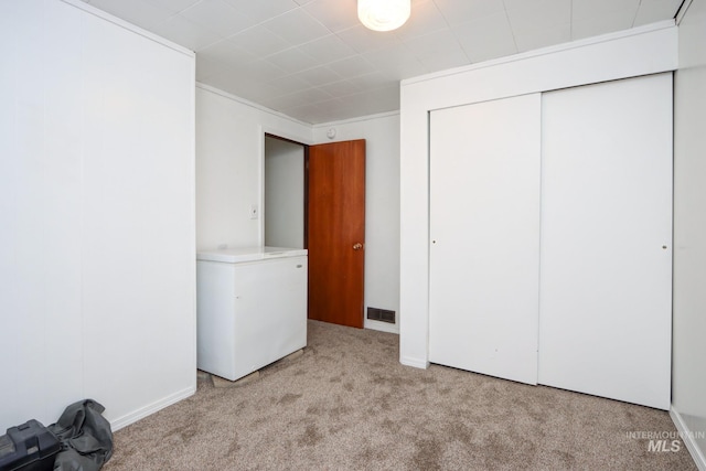 unfurnished bedroom featuring fridge, visible vents, carpet, and a closet