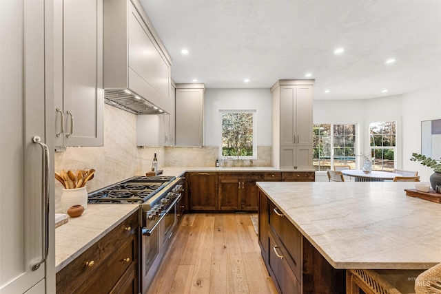 kitchen with sink, double oven range, backsplash, light stone countertops, and light wood-type flooring