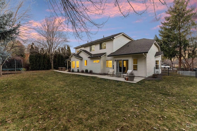 back house at dusk with a patio, a yard, and a trampoline