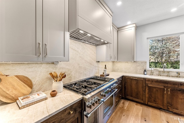 kitchen featuring sink, double oven range, tasteful backsplash, light stone countertops, and light wood-type flooring