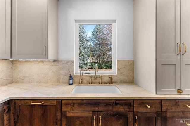 kitchen with dark brown cabinetry, light stone countertops, sink, and decorative backsplash