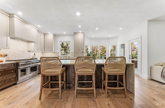 kitchen featuring light hardwood / wood-style flooring, a breakfast bar, double oven range, a center island, and decorative backsplash