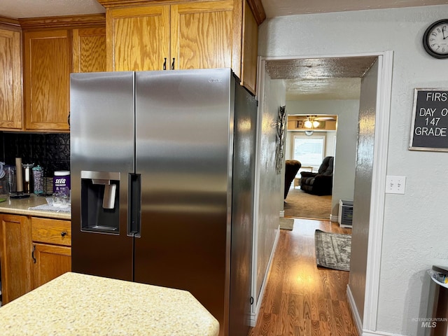 kitchen with light stone countertops, stainless steel refrigerator with ice dispenser, backsplash, and hardwood / wood-style floors