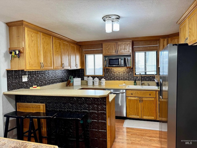 kitchen with sink, kitchen peninsula, a breakfast bar area, appliances with stainless steel finishes, and light wood-type flooring