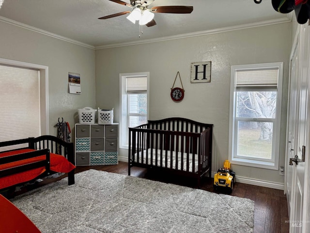 bedroom featuring dark hardwood / wood-style flooring, a nursery area, ceiling fan, and ornamental molding