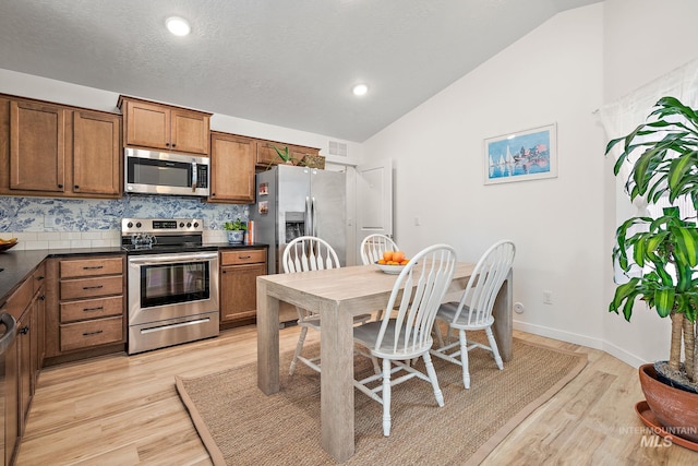 kitchen with dark countertops, vaulted ceiling, brown cabinets, and stainless steel appliances