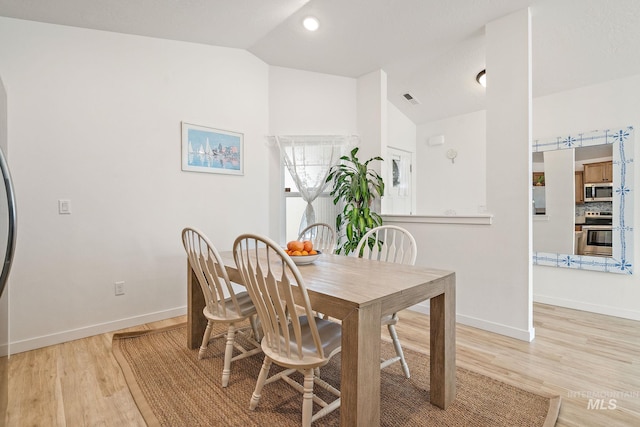 dining space with light wood-type flooring, visible vents, vaulted ceiling, and baseboards