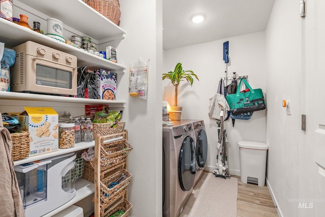 clothes washing area with laundry area, baseboards, wood finished floors, and washing machine and clothes dryer