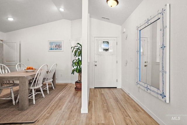 foyer entrance with light wood-type flooring, lofted ceiling, visible vents, and baseboards