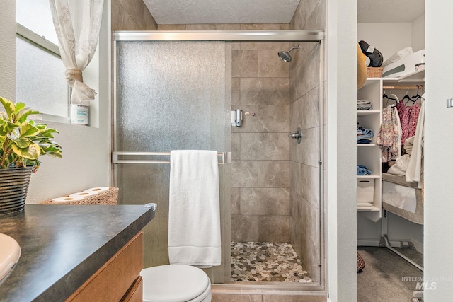 bathroom featuring a textured wall, toilet, vanity, a spacious closet, and a shower stall