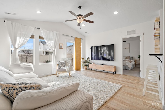 living room with lofted ceiling, visible vents, ceiling fan, and light wood finished floors