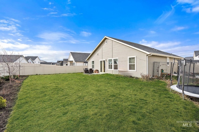 back of house featuring a trampoline, a fenced backyard, a yard, and a patio