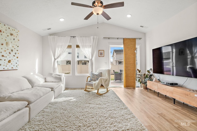 living area with lofted ceiling, a textured ceiling, visible vents, and light wood-style floors