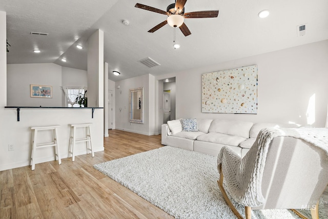 living area featuring lofted ceiling, wood finished floors, visible vents, and a ceiling fan