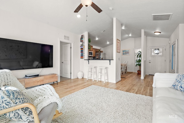 living room with a ceiling fan, visible vents, vaulted ceiling, and wood finished floors