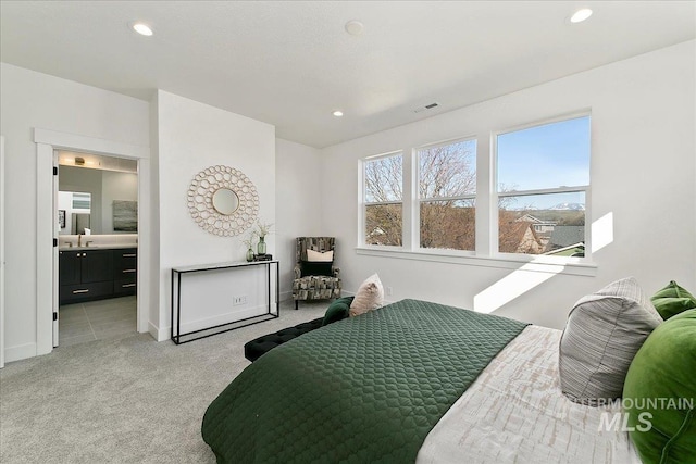 bedroom with light colored carpet, ensuite bathroom, and sink