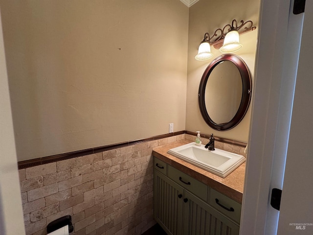 bathroom featuring a wainscoted wall, brick wall, and vanity