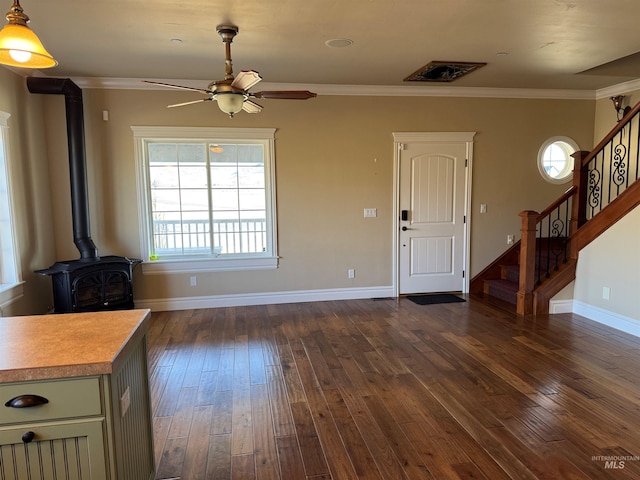 unfurnished living room with baseboards, stairway, dark wood finished floors, a wood stove, and crown molding