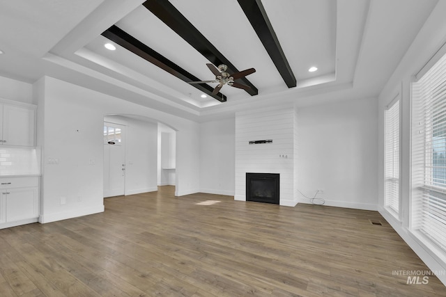 1734 Shoal Point Ave, Middleton, ID 83644 - unfurnished living room featuring a large fireplace, a raised ceiling, light wood-style floors, ceiling fan, and arched walkways