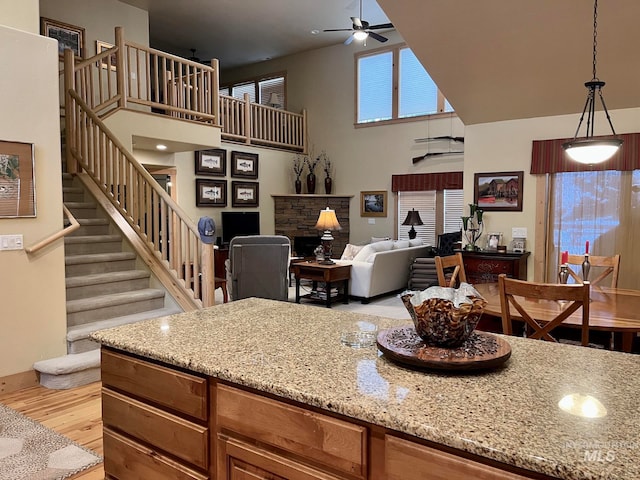 kitchen with pendant lighting, ceiling fan, light stone countertops, a towering ceiling, and light hardwood / wood-style floors