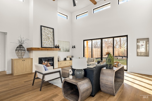 living room with beamed ceiling, a towering ceiling, light hardwood / wood-style flooring, and ceiling fan