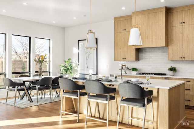 kitchen with stainless steel gas stovetop, light hardwood / wood-style floors, an island with sink, and hanging light fixtures