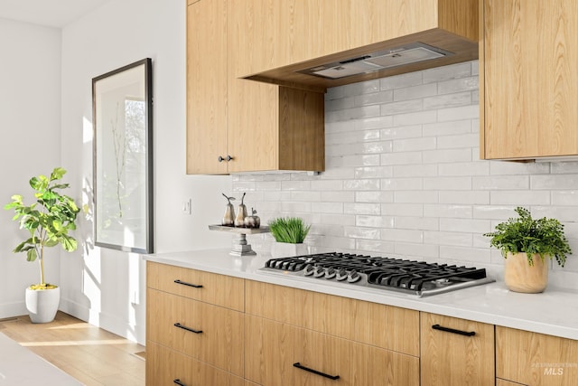 kitchen featuring decorative backsplash, light brown cabinetry, light wood-type flooring, custom exhaust hood, and stainless steel gas stovetop