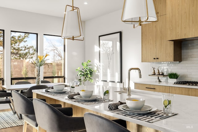 kitchen featuring light stone countertops, tasteful backsplash, pendant lighting, hardwood / wood-style floors, and stainless steel gas stovetop