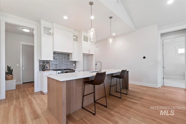 6874 N Fireball, Meridian, ID 83646 - kitchen featuring a sink, light wood-style flooring, a center island with sink, decorative backsplash, and white cabinets