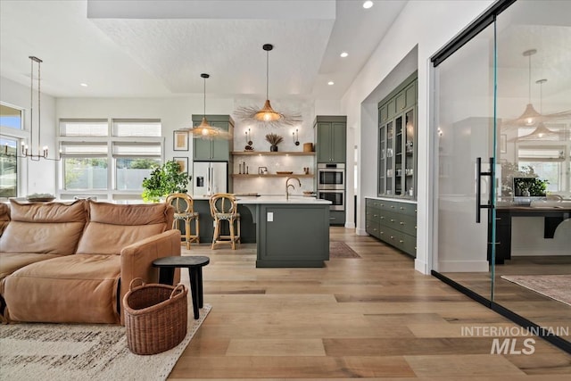 bar featuring refrigerator with ice dispenser, light wood-style flooring, recessed lighting, a sink, and stainless steel double oven