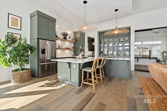 kitchen with appliances with stainless steel finishes, light countertops, light wood-type flooring, open shelves, and hanging light fixtures