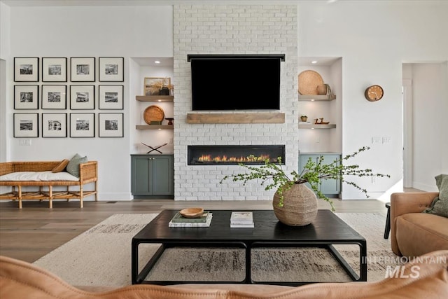 living room featuring a brick fireplace, wood finished floors, built in features, and baseboards