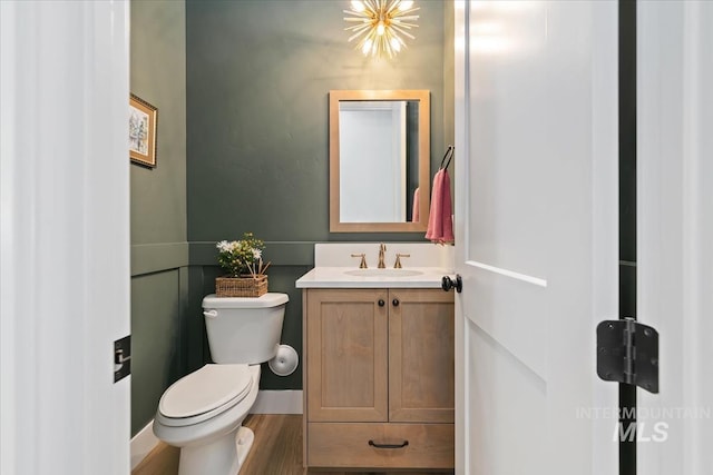 half bathroom with toilet, vanity, and wood finished floors
