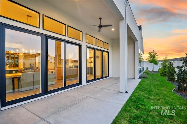exterior entry at dusk with ceiling fan, a patio area, and stucco siding