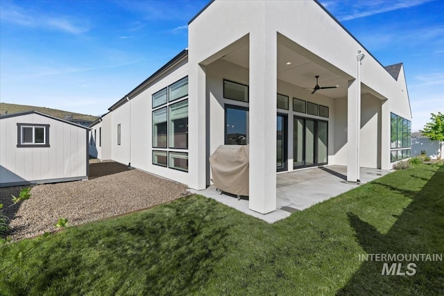 back of property with a ceiling fan, a patio area, a lawn, and stucco siding
