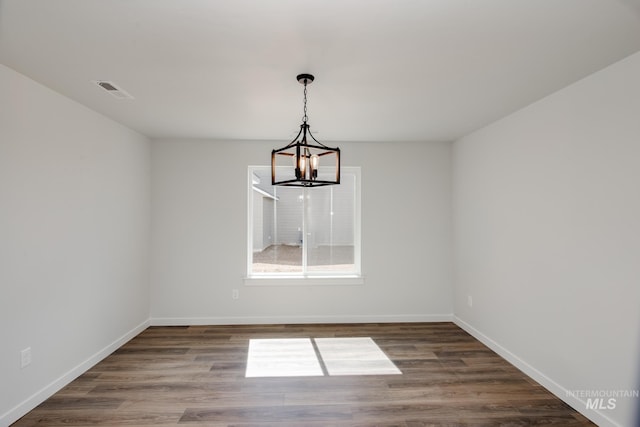 empty room with an inviting chandelier, visible vents, baseboards, and wood finished floors