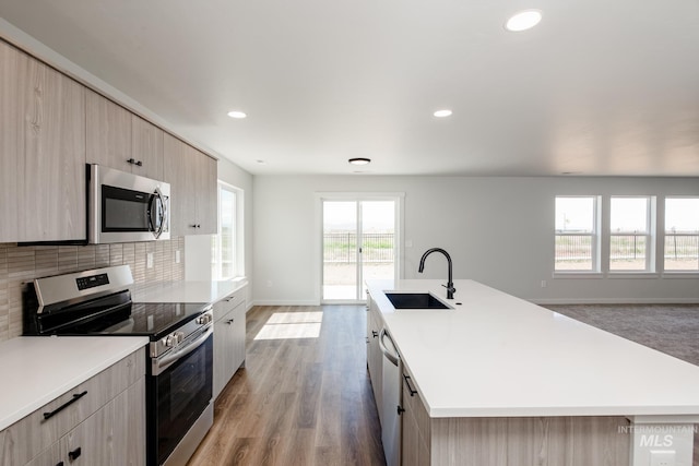 kitchen featuring a sink, light countertops, appliances with stainless steel finishes, backsplash, and an island with sink